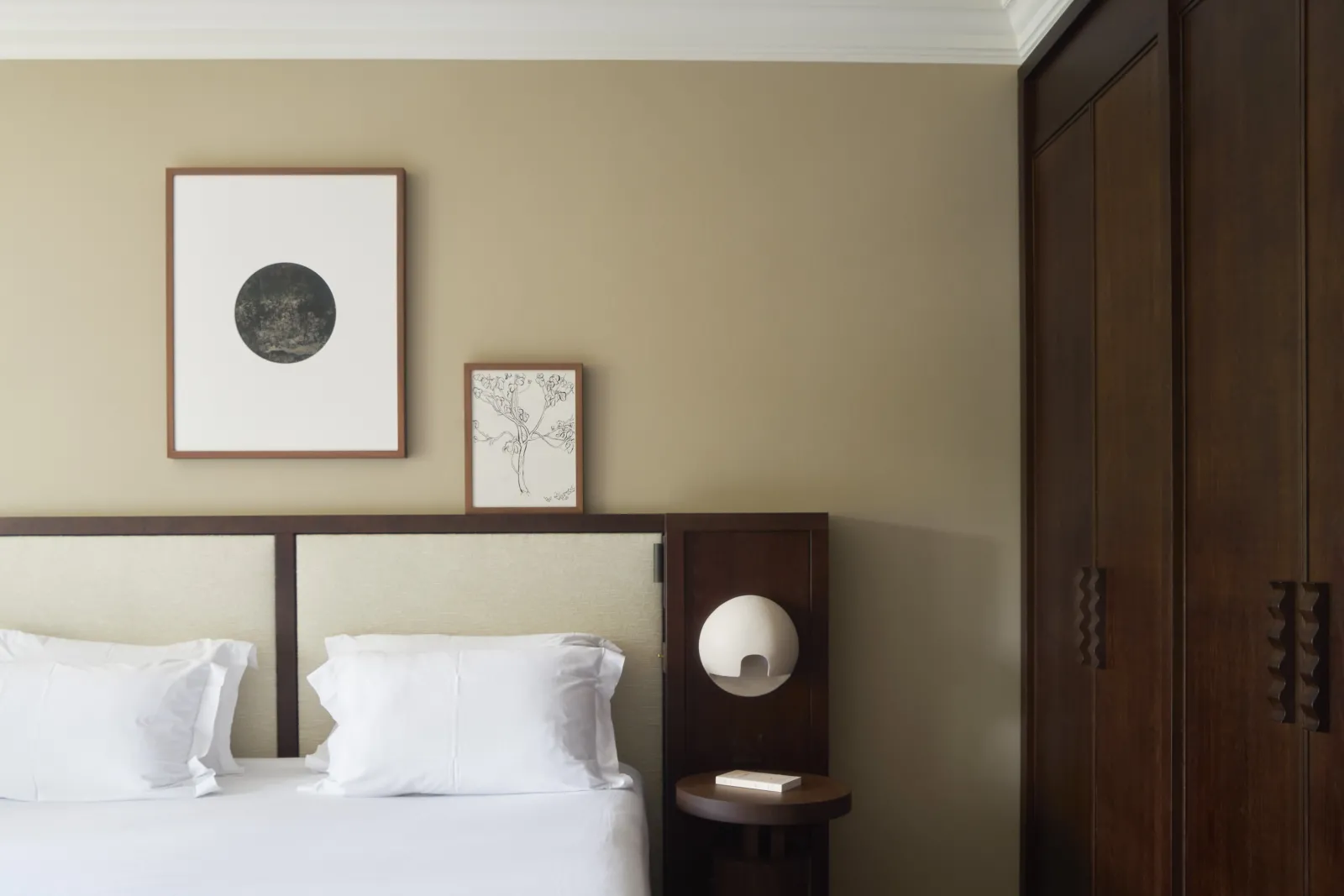 Elegant bedroom at Les Sources de Caudalie in Bordeaux featuring a wood-framed bed, light beige walls, two framed artworks above the headboard, and dark brown wardrobe