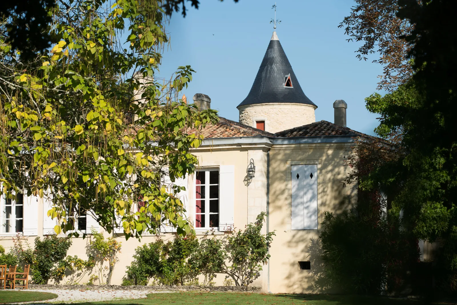 Château Latour-Martillac in Bordeaux, white building with a pointed turret topped with a black roof, surrounded by greenery and vineyards