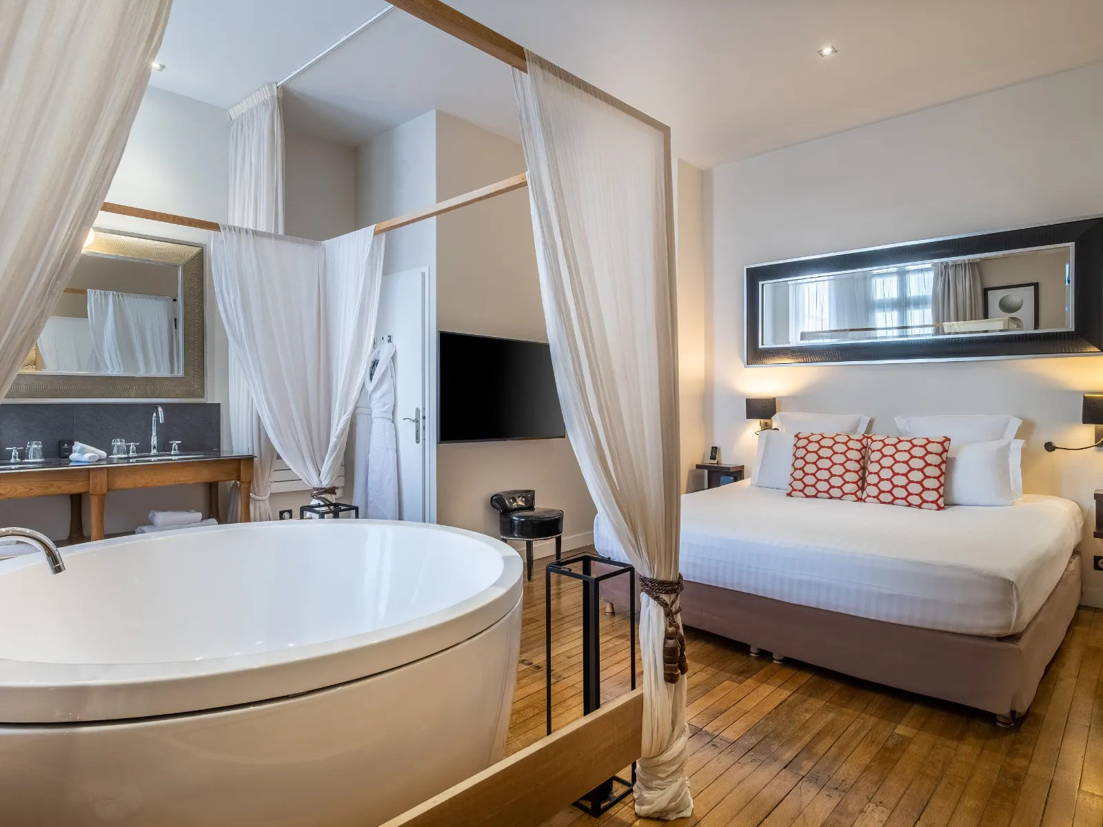 Luxury hotel suite in Bordeaux featuring a canopy bed, round marble bathtub, integrated bathroom, and modern décor with neutral and gold tones.