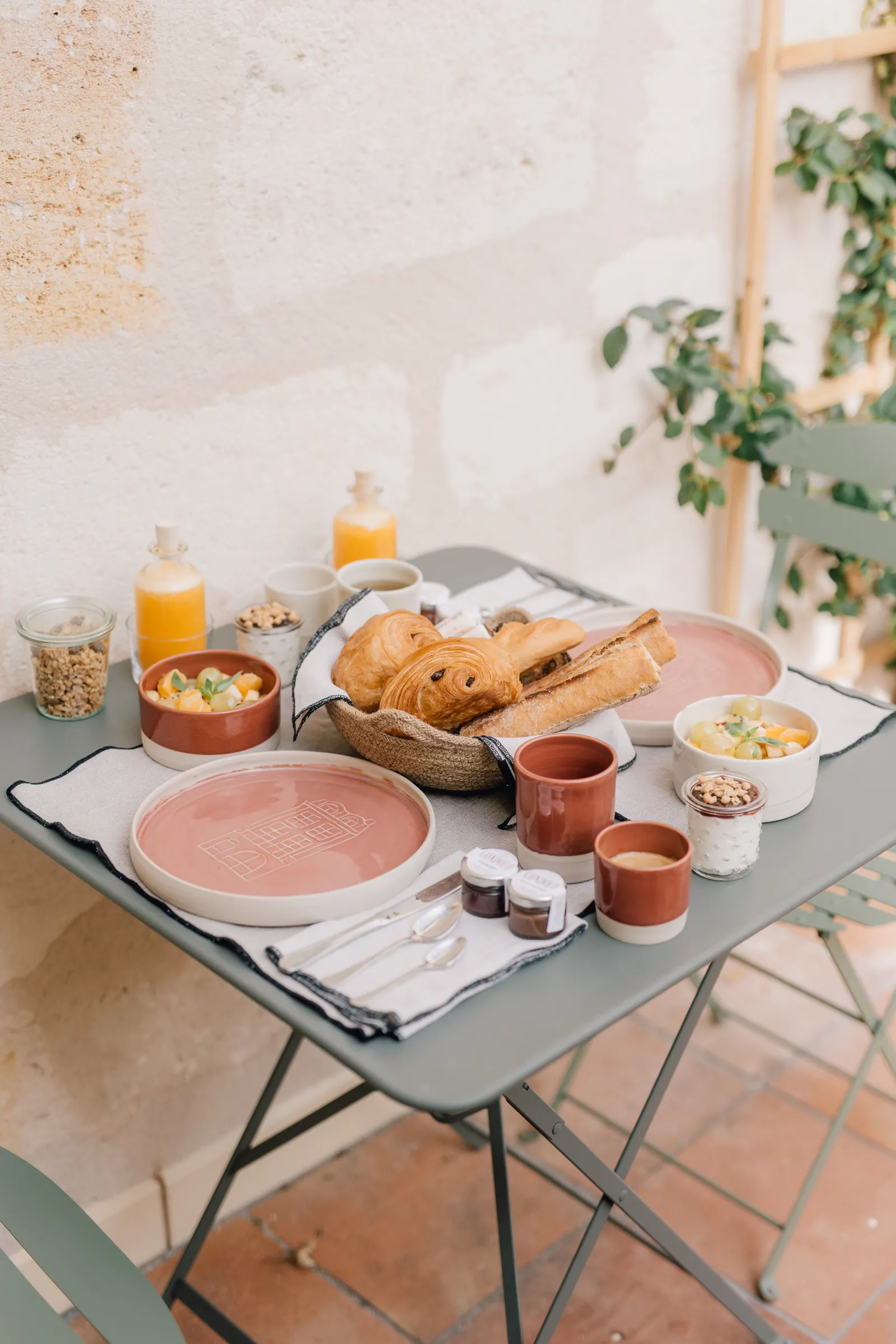 Elegant breakfast table setting with pink plates, fresh bread, orange juice, cereals and tableware in a bright minimalist setting