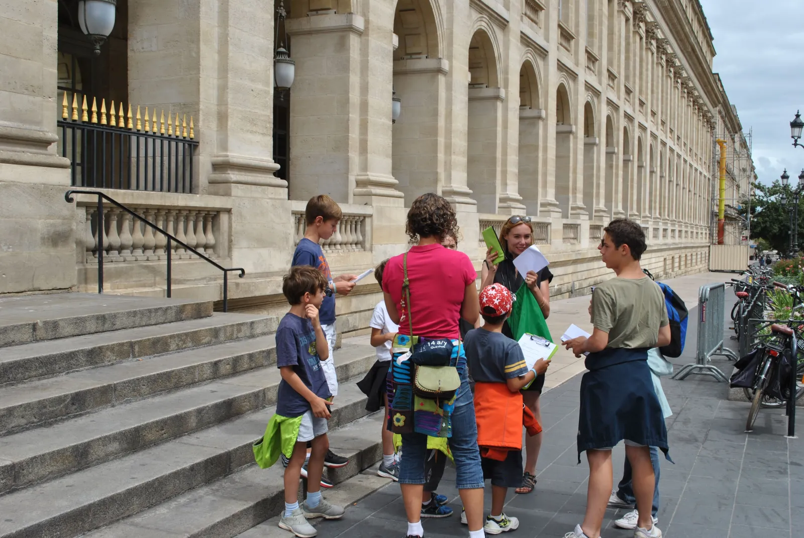 A group of children on a guided tour in front of a classical historic building facade in Bordeaux, consulting tourist documents.