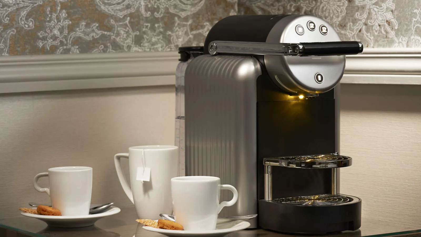 Modern Nespresso capsule coffee machine with three white cups and cookies arranged on a table in an elegant hotel setting.