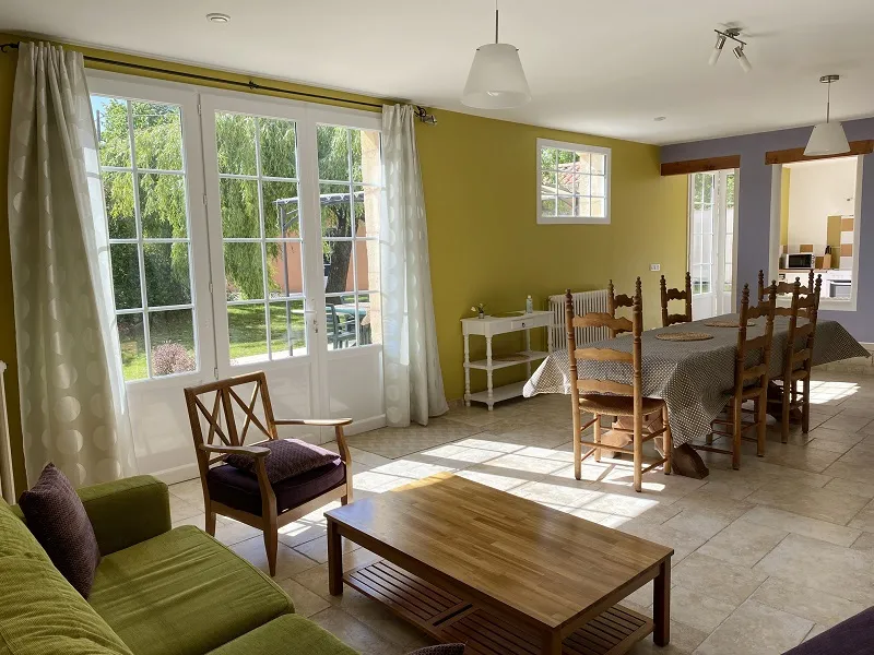 Spacious living room at Château La Gontrie featuring wooden furniture, yellow and purple walls, large glass doors overlooking the garden, and adjacent dining area