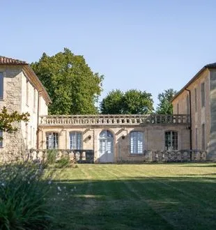 Courtyard view of Château de Ferrand in Bordeaux featuring stone buildings with balustrades and green lawn under clear blue sky.