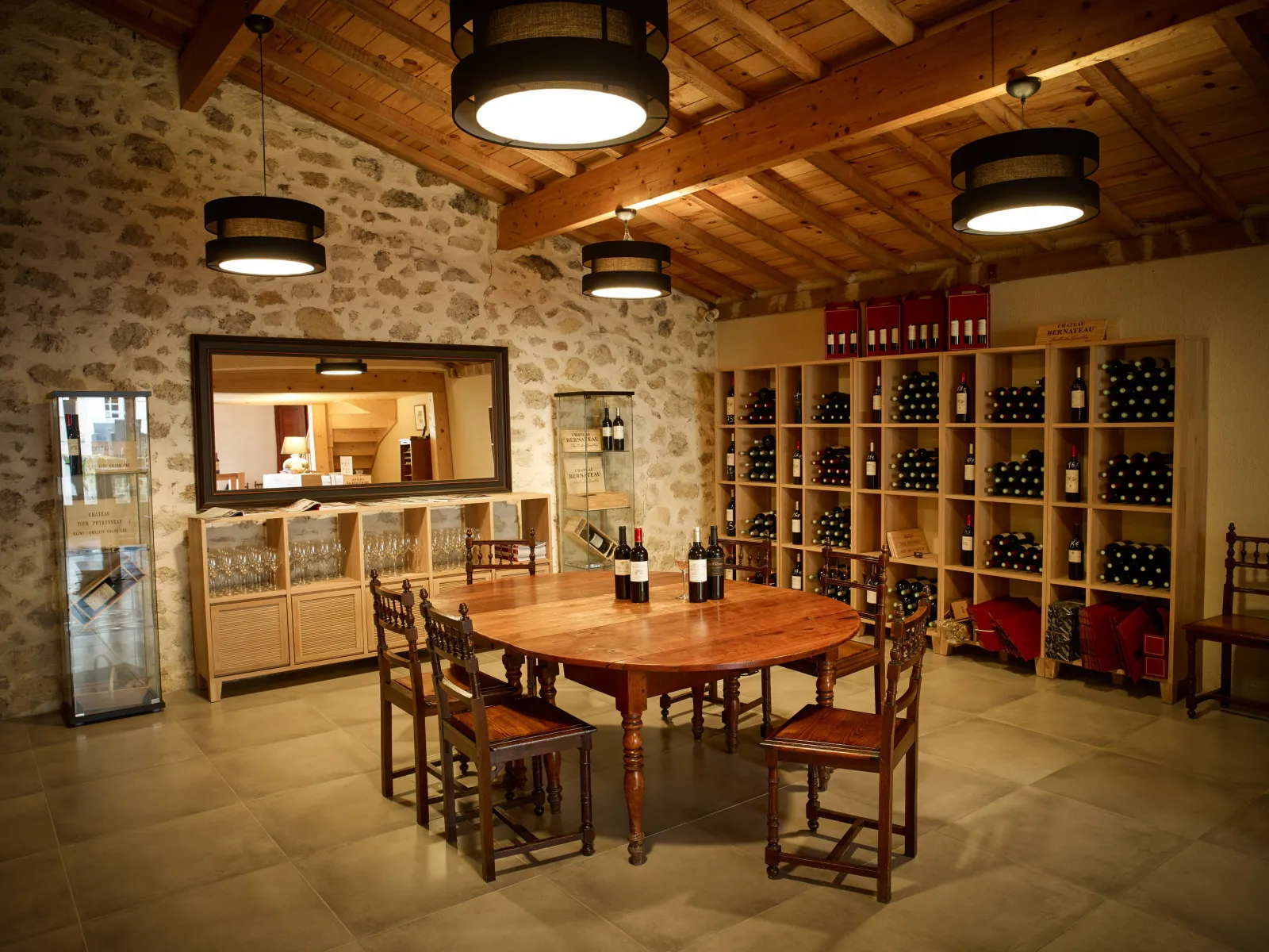 Elegant wine cellar interior with wooden tasting table, carved wooden chairs, storage shelves filled with wine bottles, bar with mirror and counter, exposed stone walls, wooden ceiling with exposed beams and modern lighting fixtures.