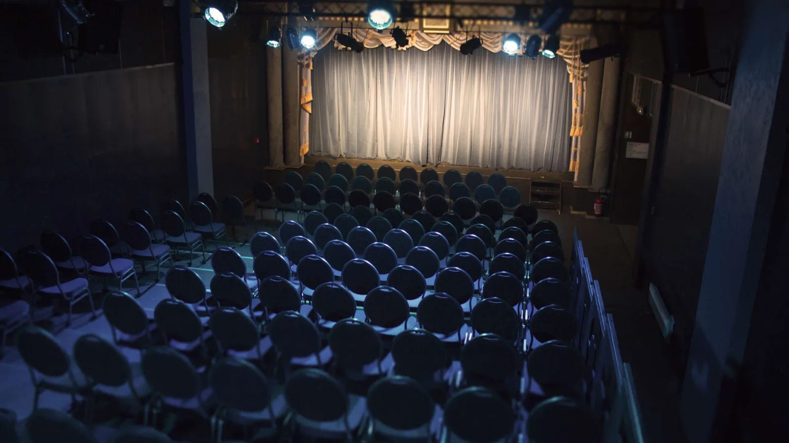 Empty theater auditorium with rows of black seats facing an illuminated stage with white and gold curtains in Bordeaux