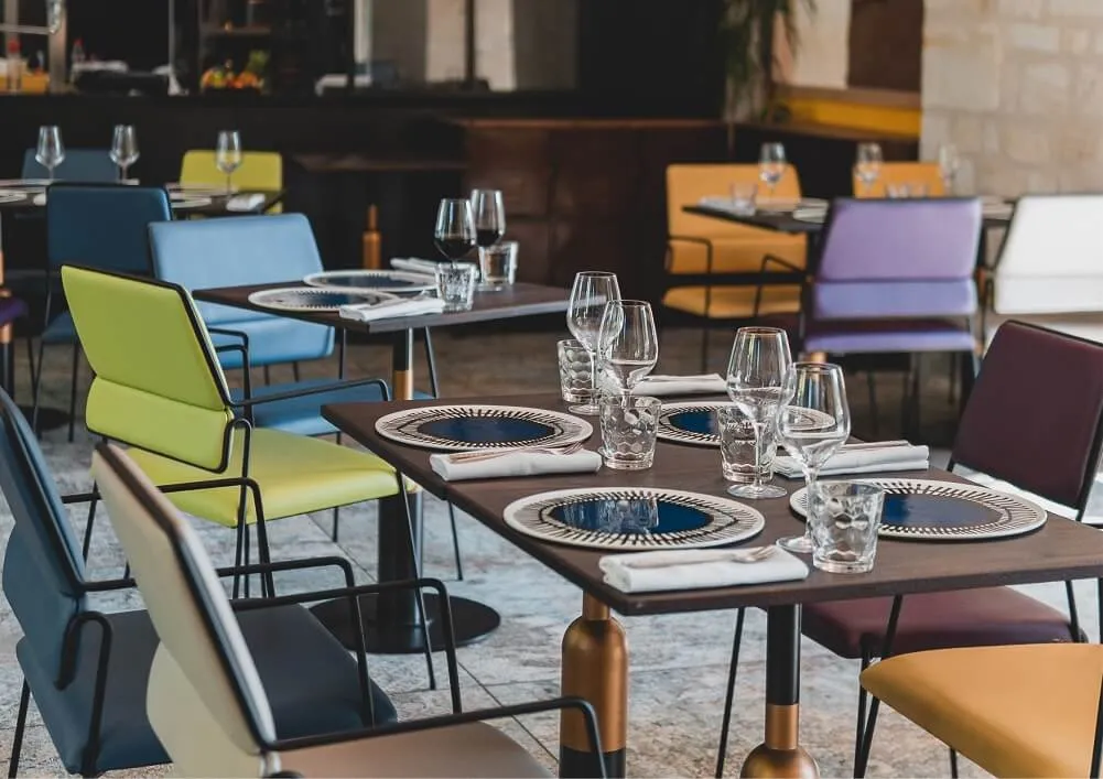 Modern restaurant interior with set tables, colorful chairs in yellow, blue, orange and purple, and elegant tableware at La Zoologie hotel restaurant in Bordeaux.