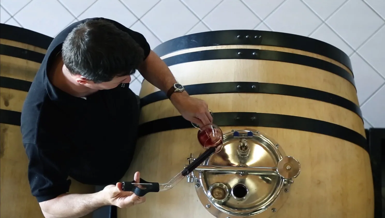 A man samples wine from a wooden barrel with metal bands at Château La Rose Perrière in Bordeaux.