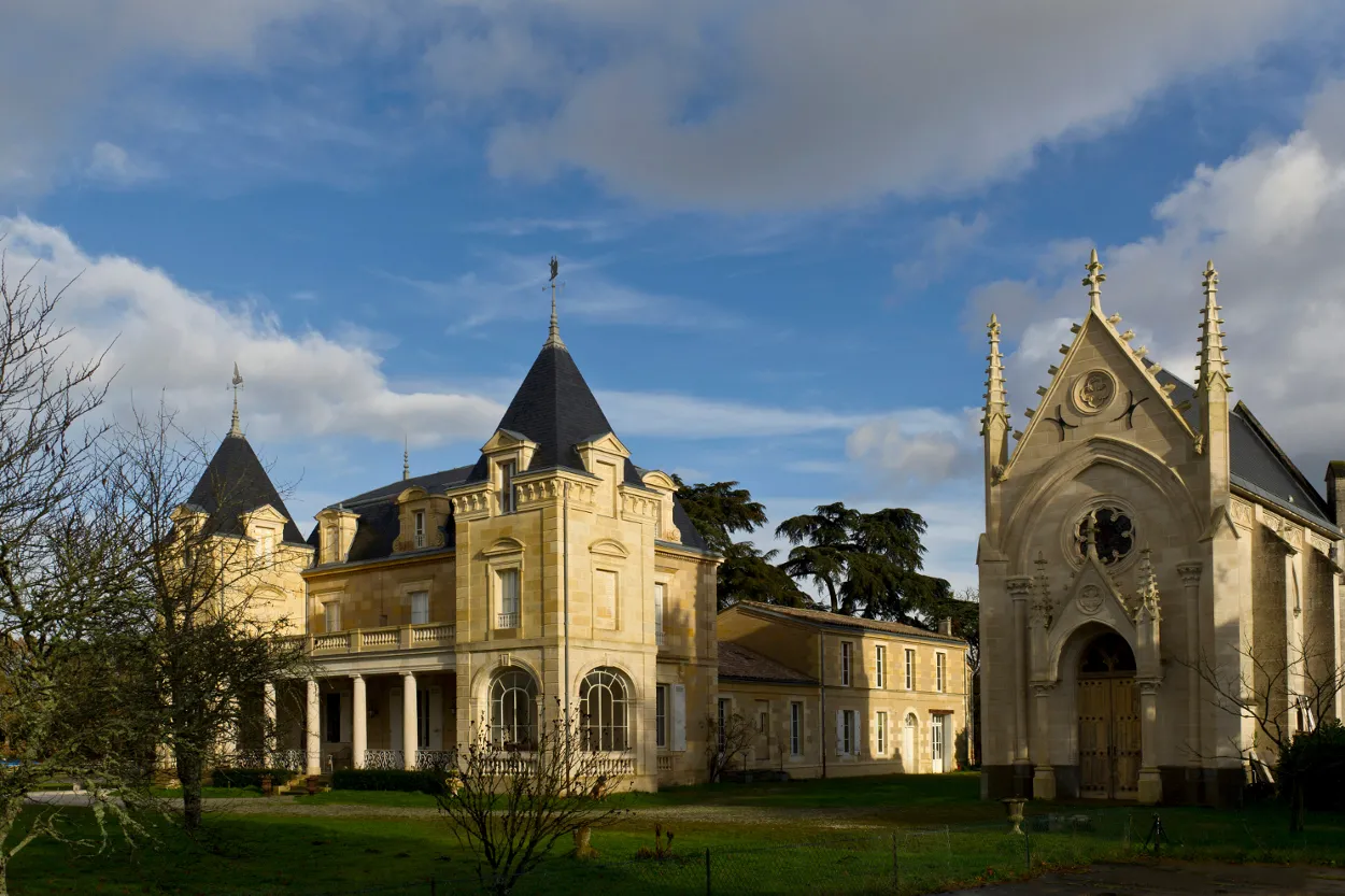 Château Léognan near Bordeaux, featuring a Second Empire mansion with pointed turrets and an adjacent Gothic chapel, surrounded by lawns and trees under a partly cloudy sky.