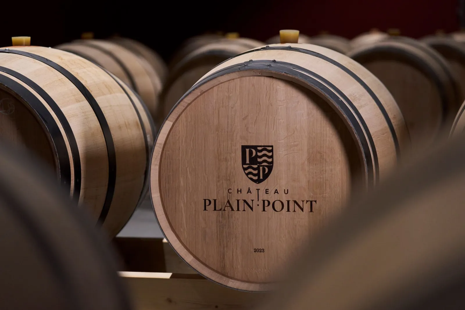 Row of oak barrels from Château Plain Point in Bordeaux, with vintage 2023 engraved on the front barrel