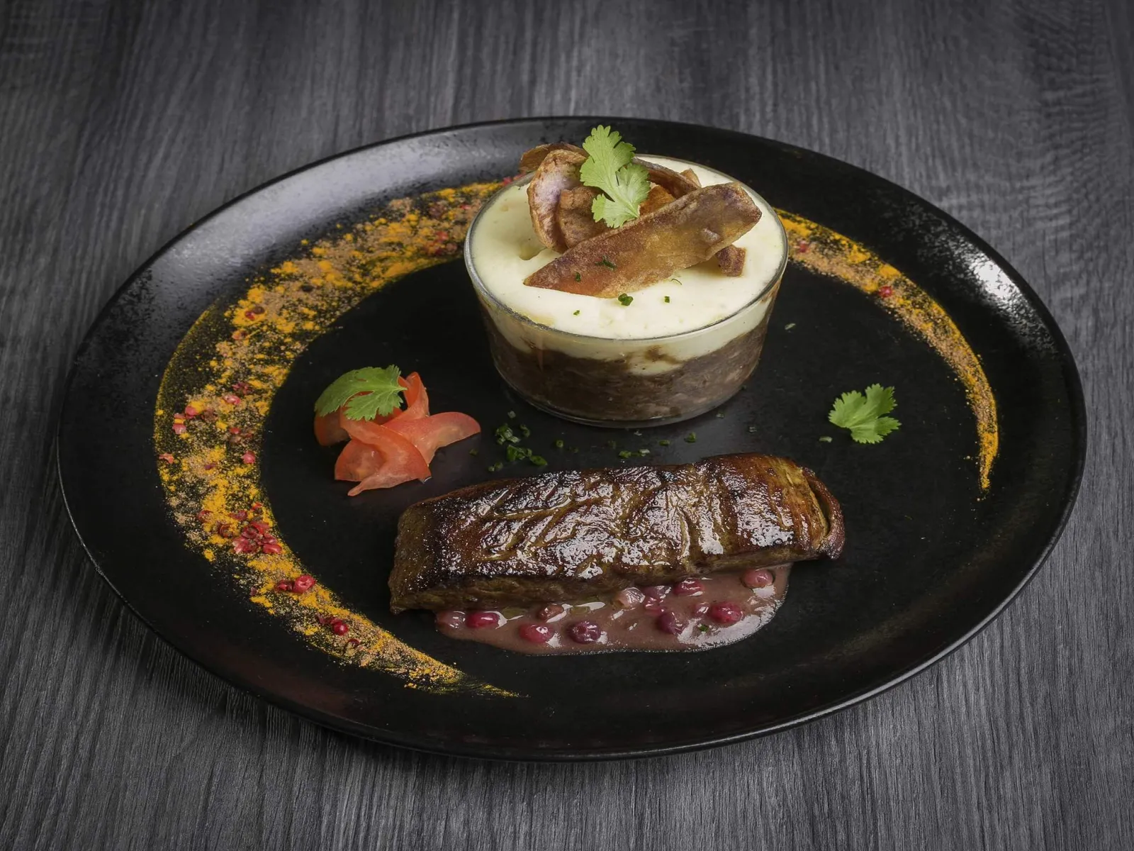 Black gourmet plate featuring seared foie gras with red berry sauce, a cylinder of foie gras mousse and golden reduction, garnished with fresh cilantro and pan-fried ginger slices