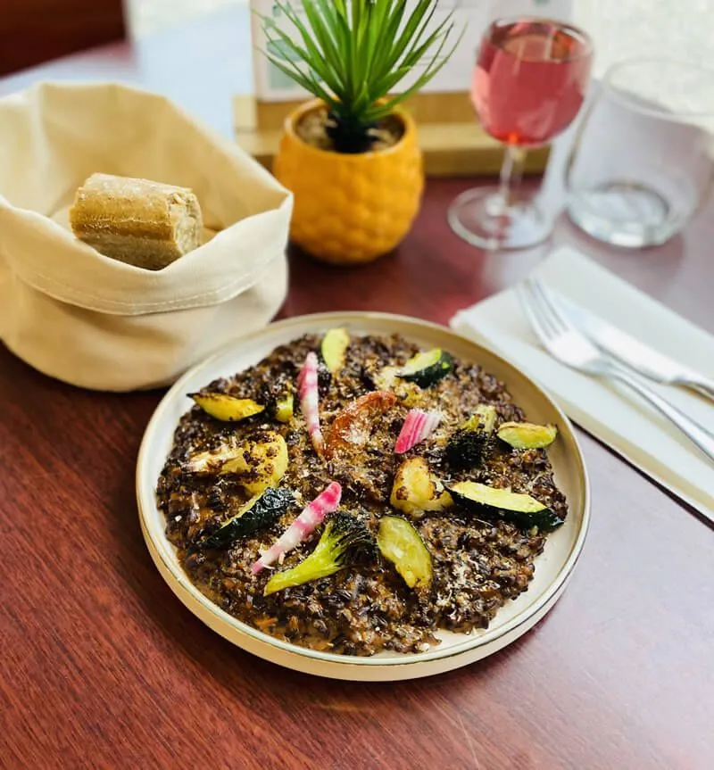 Black seafood risotto plate garnished with zucchini and rhubarb, served at Soretel restaurant in Bordeaux Mérignac, with bread, rosé wine and floral decoration