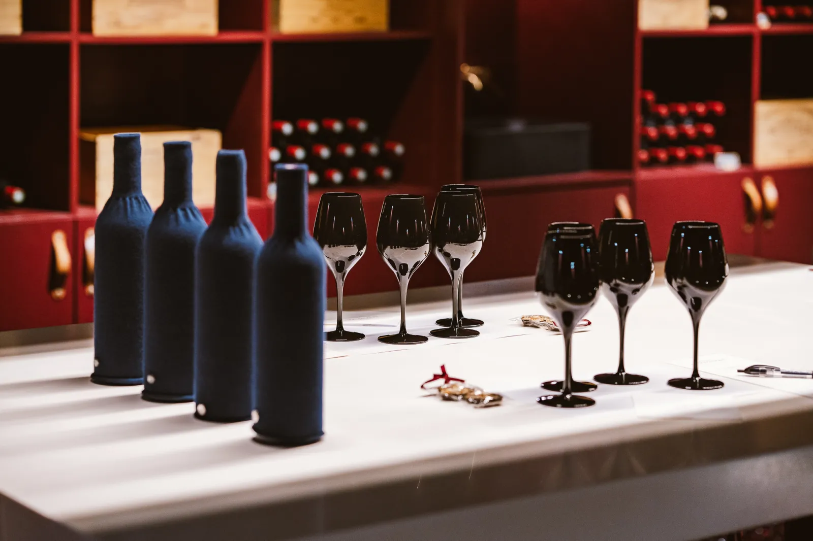 Wine tasting at Château La Dominique in Bordeaux: four red wine bottles and six black glasses arranged on a white table, with a wine cellar in the background.