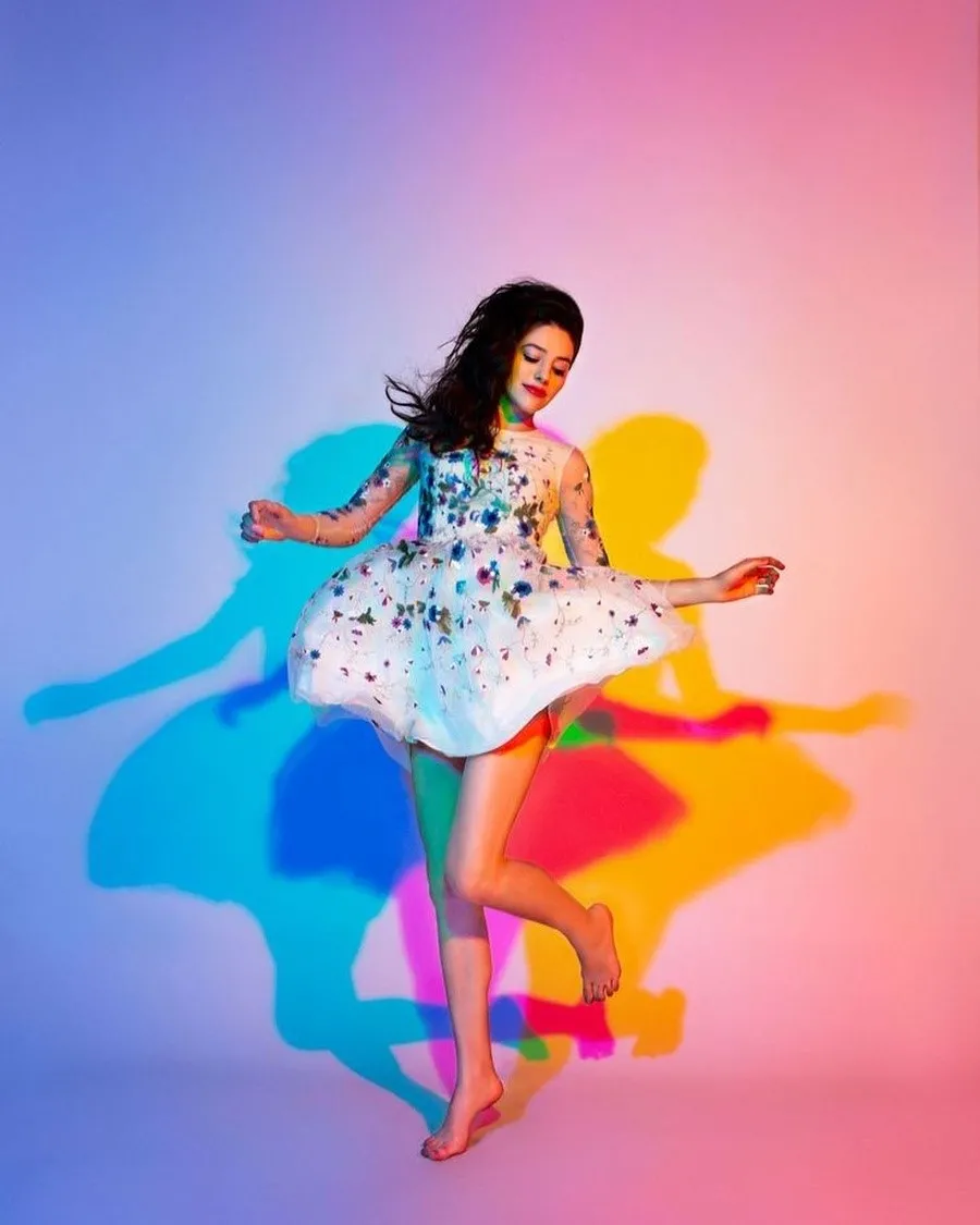 Young woman in a white sequined dress dancing against a pink and blue gradient background with stylized colorful shadows