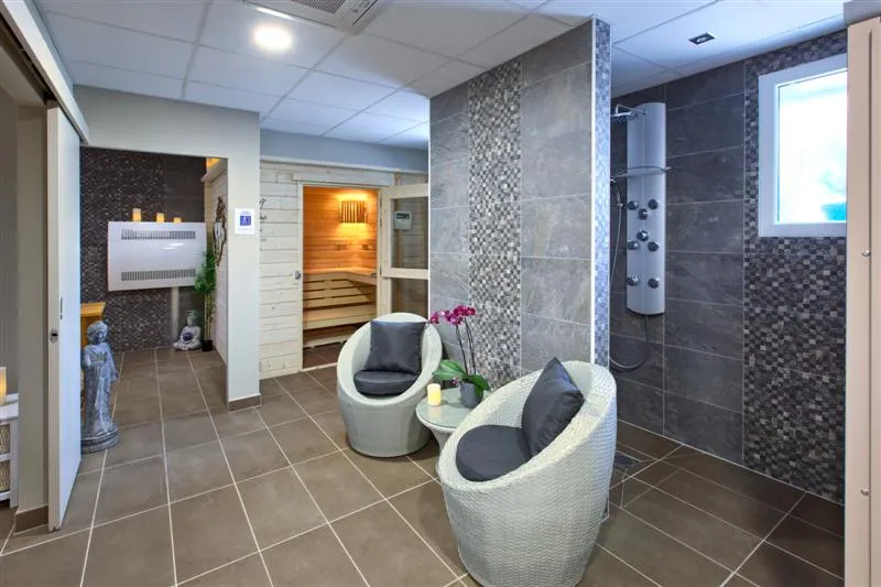 Modern spa facility featuring a wooden sauna, jet shower, two comfortable white armchairs, and gray tiling at Hôtel Au Comté d'Ornon in Bordeaux.
