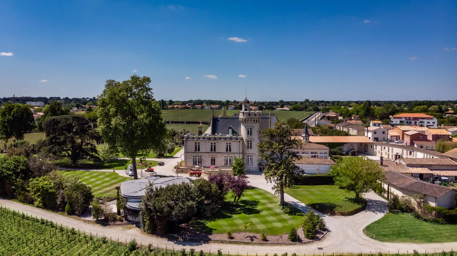 Aerial view of Château Pape Clément in Bordeaux, a white neo-Gothic castle surrounded by vineyards, manicured gardens and outbuildings in the Bordeaux wine region.