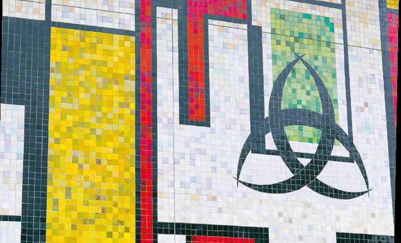 Colorful tile mosaic wall at the Grand Parc Event Hall in Bordeaux, featuring small square tiles arranged in geometric patterns: a yellow square, red and green bands, and a black triangular symbol on a light background.