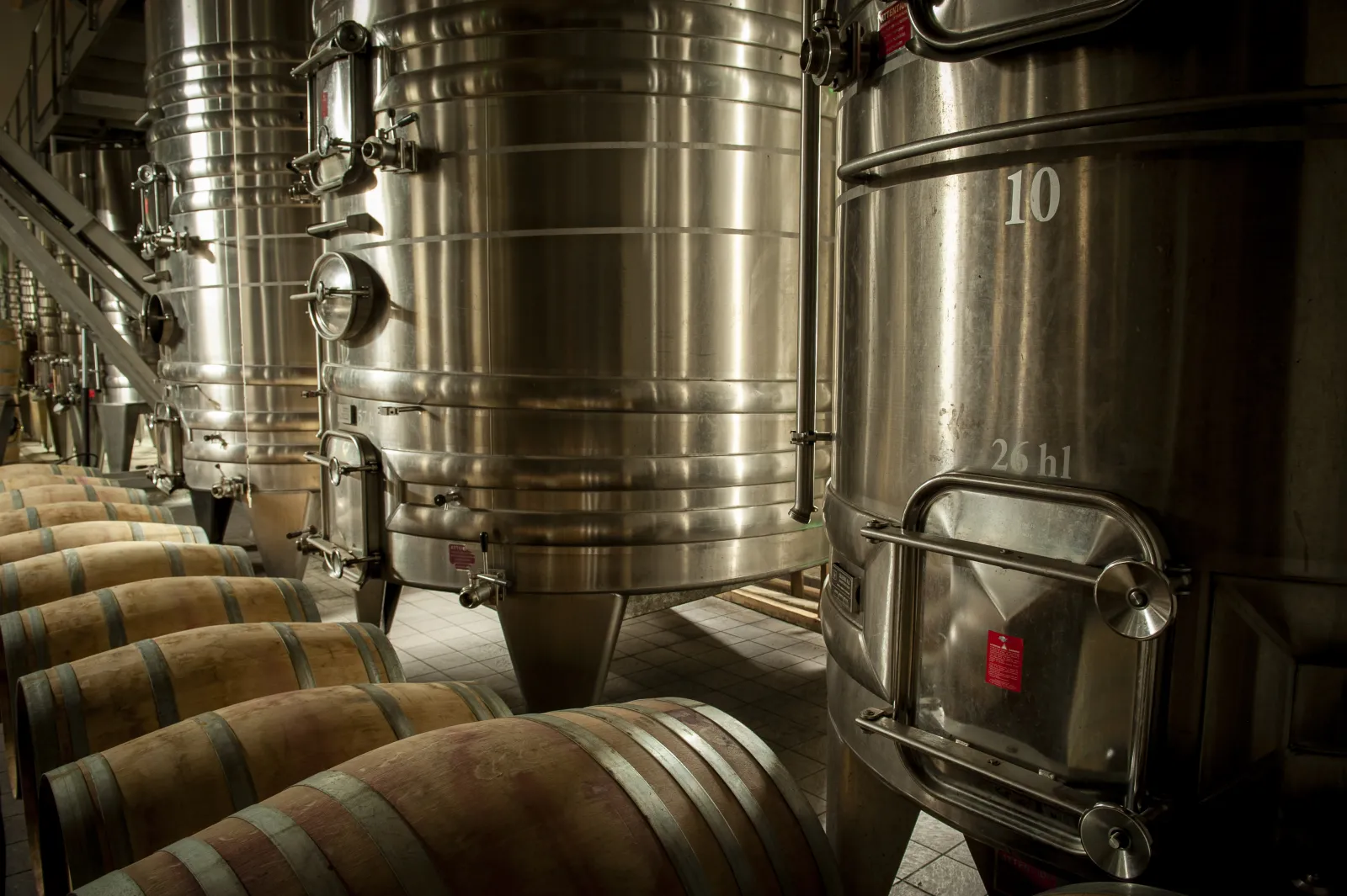 Wine cellar at Château Couhins in Bordeaux featuring wooden barrels in the foreground and stainless steel fermentation tanks in the background