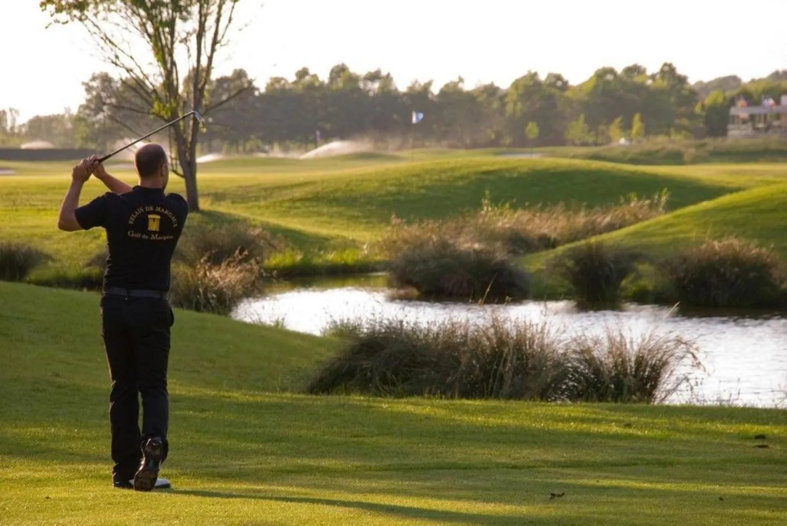 Golfer taking a swing on the Margaux Golf course with ponds and woodland in the background
