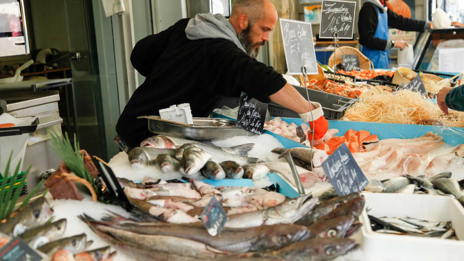 Fishmonger at Bordeaux's Capucins Market displaying fresh fish and seafood stall with price labels