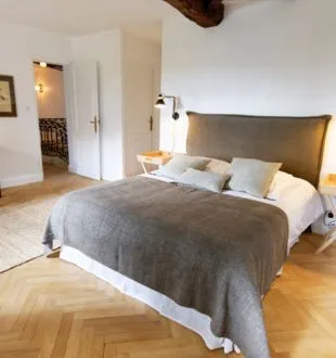 Spacious bedroom featuring a double bed with gray throw, golden headboard, herringbone parquet flooring, white doors, exposed beam and minimalist furnishings at Maison La Fleur de Boüard in Bordeaux