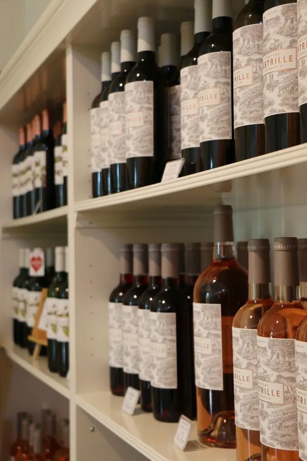 White shelves displaying a collection of wine bottles from Château Lestrille in Bordeaux, featuring gray labels and bottles in various colors from red to rosé.