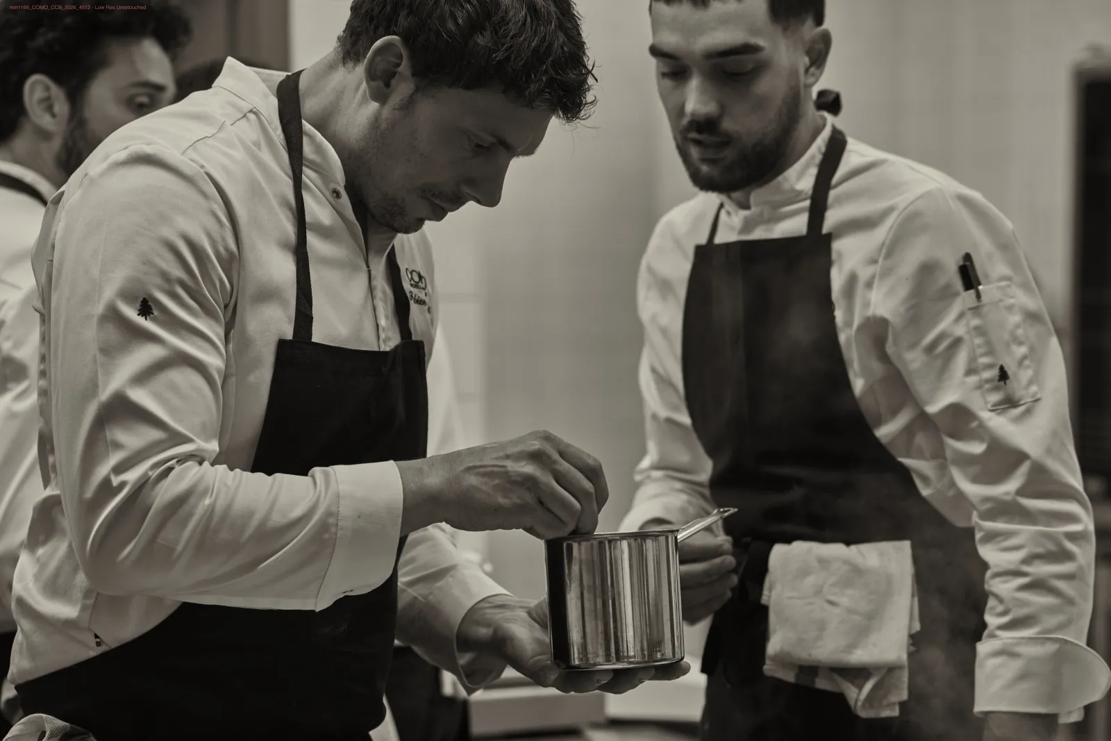 Three professional chefs in white chef coats and black aprons carefully inspect a baking mold in a professional kitchen in Bordeaux.