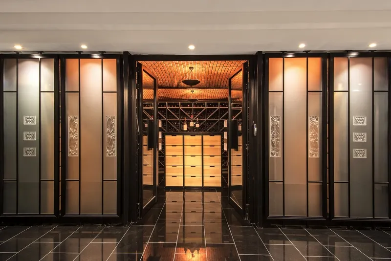 Elegant entrance of Lalique restaurant at Château Lafaurie Peyraguey in Bordeaux, featuring glass doors with black frames and warm golden-orange interior lighting