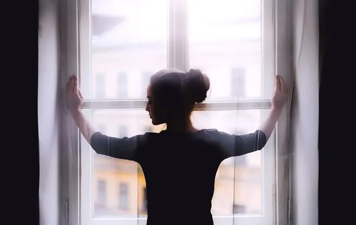 Silhouette of a woman from behind with arms outstretched, looking out a large window overlooking the city of Bordeaux