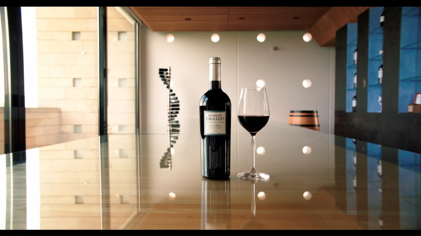Bottle of Château Faugères and glass of red wine in a modern interior overlooking Bordeaux