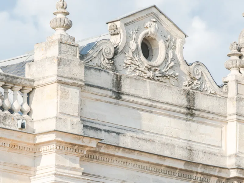 Architectural detail of Château Giscours in Bordeaux featuring an ornamental white stone cornice with sculpted scrolls, a circular opening, and floral motifs characteristic of classical Bordeaux architecture.