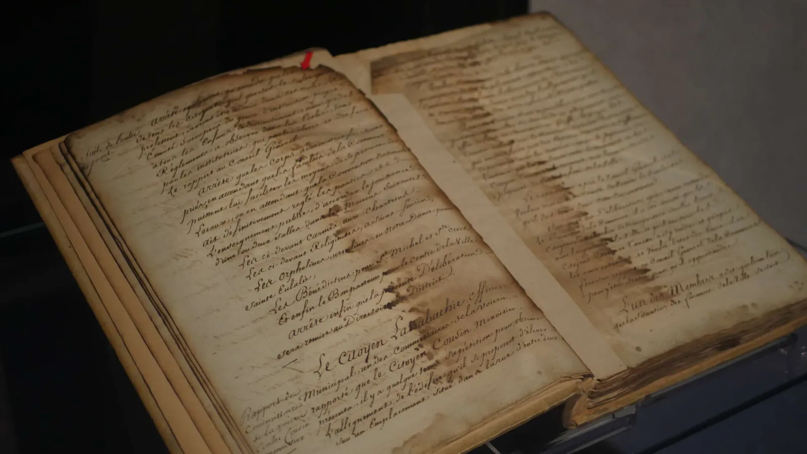 Open antique book displaying two handwritten pages in French from Bordeaux historical archives, with a red ribbon bookmark.
