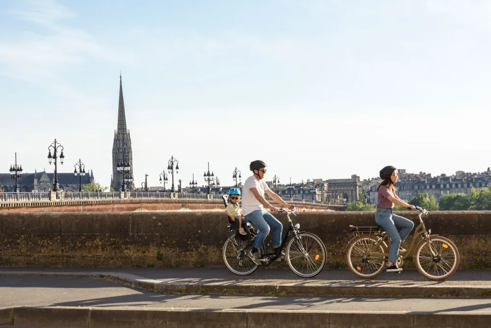 Three cyclists riding bikes along Bordeaux waterfront with Saint-Michel Basilica in the background