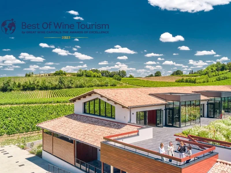 Maison Cardinale in Bordeaux, a modern building with panoramic terrace overlooking Bordeaux vineyards under clear blue sky. Best of Wine Tourism 2023 logo visible.