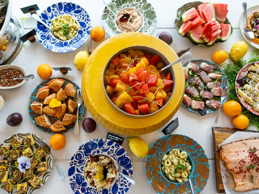 Festive table in Bordeaux featuring a central yellow bowl of ratatouille surrounded by decorated plates with dried fruits, fresh watermelon, cured meats, smoked fish, and various culinary preparations