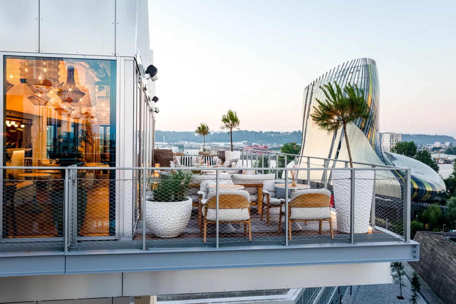 Modern rooftop terrace in Bordeaux featuring designer furniture, illuminated glass doors, palm trees and panoramic city views