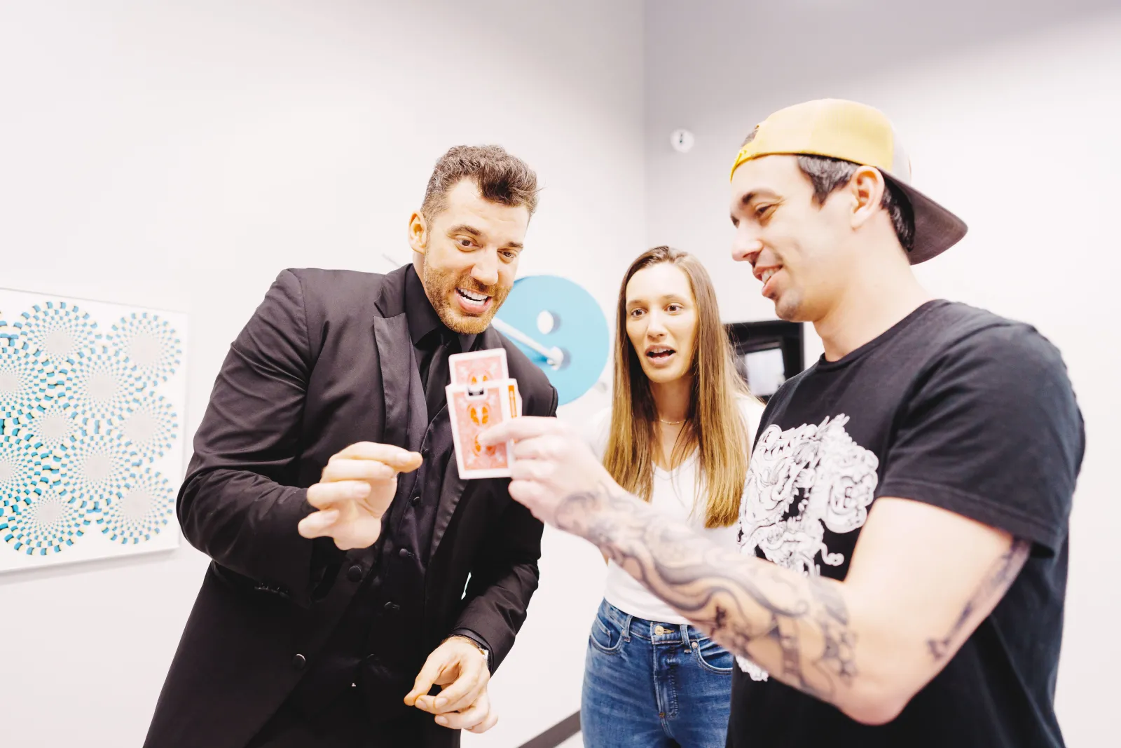 Four smiling people examining an optical illusion on a smartphone at the Museum of Illusion in Bordeaux, with geometric artwork visible in the background.