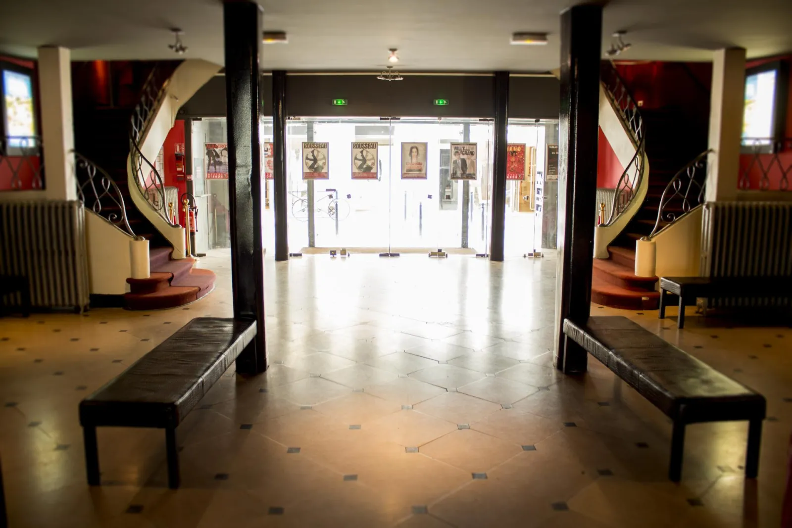 Entrance hall of Bordeaux's Trianon Theatre featuring glass doors, black columns, benches and theatrical posters, Art Deco style