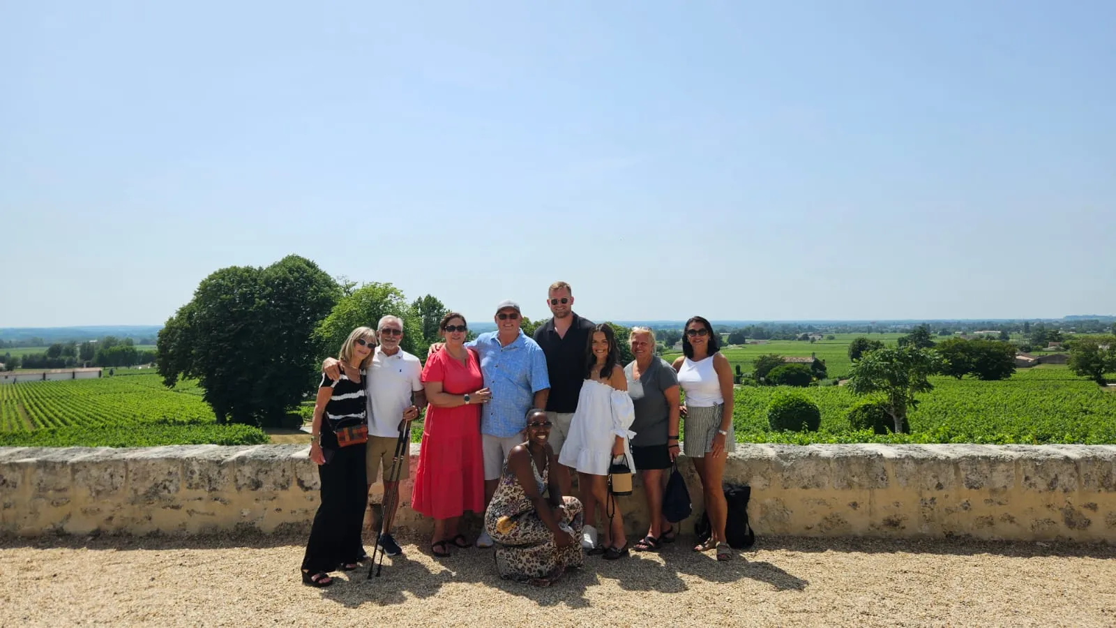 Group of tourists posing in front of Bordeaux vineyards with a stone wall and lush vineyard rows in the background