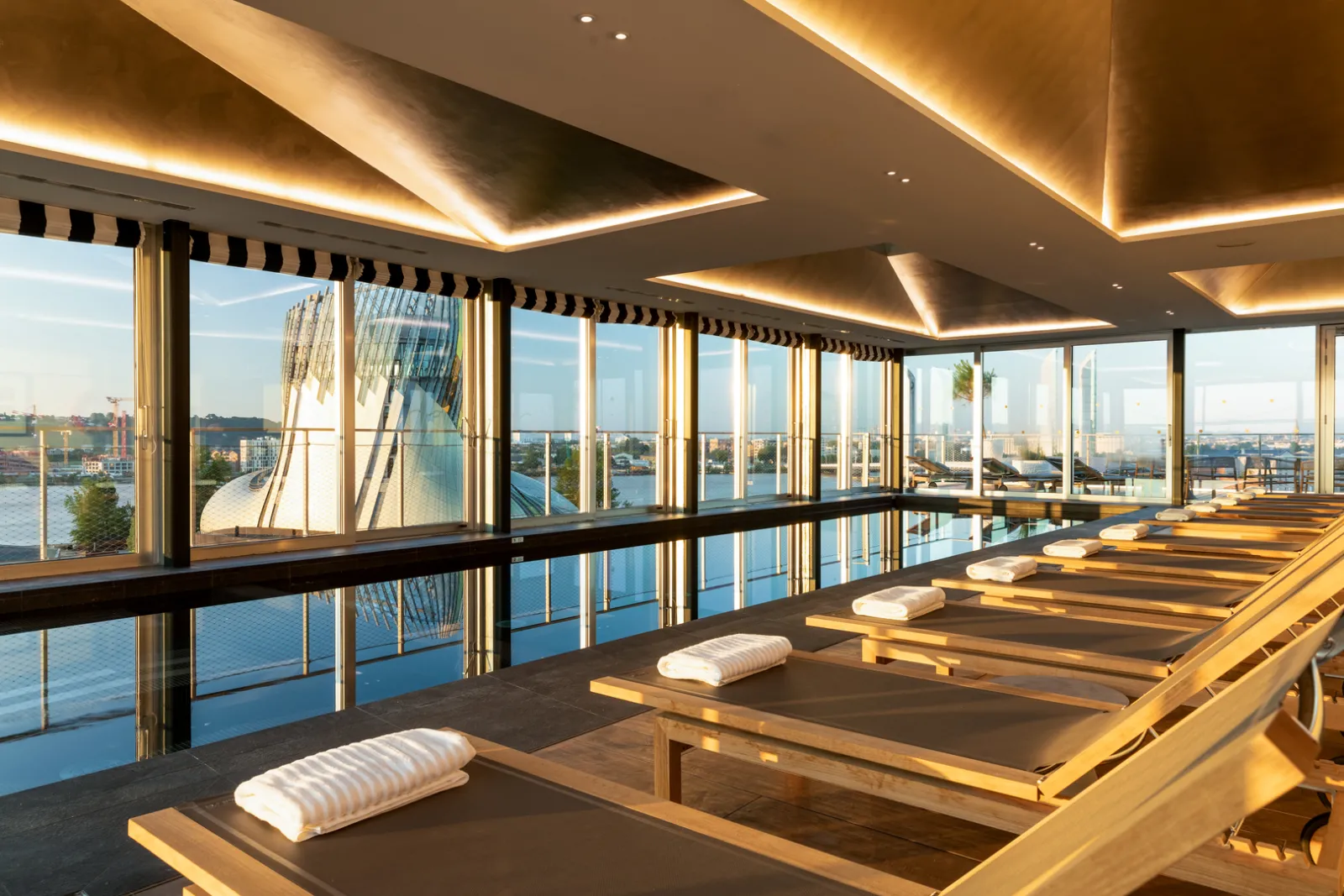 Luxury yoga studio with panoramic views of Bordeaux, yoga mats lined up, floor-to-ceiling windows overlooking the Garonne River and city skyline, modern ceiling with golden accent lighting