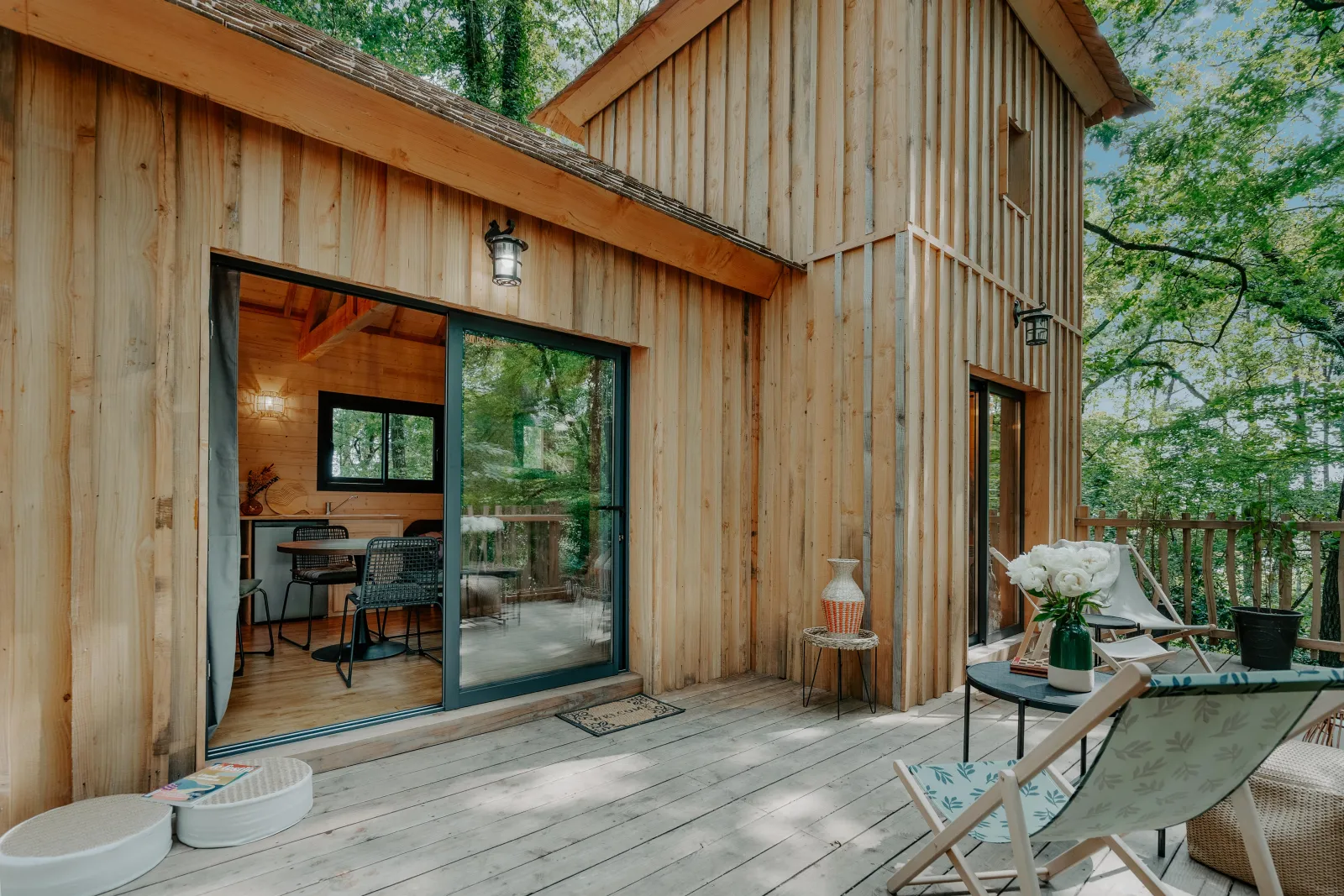 Modern Gironde cabin featuring a wooden deck terrace, light wood cladding exterior, large glass doors, relaxation furniture, and surrounded by natural greenery near Bordeaux