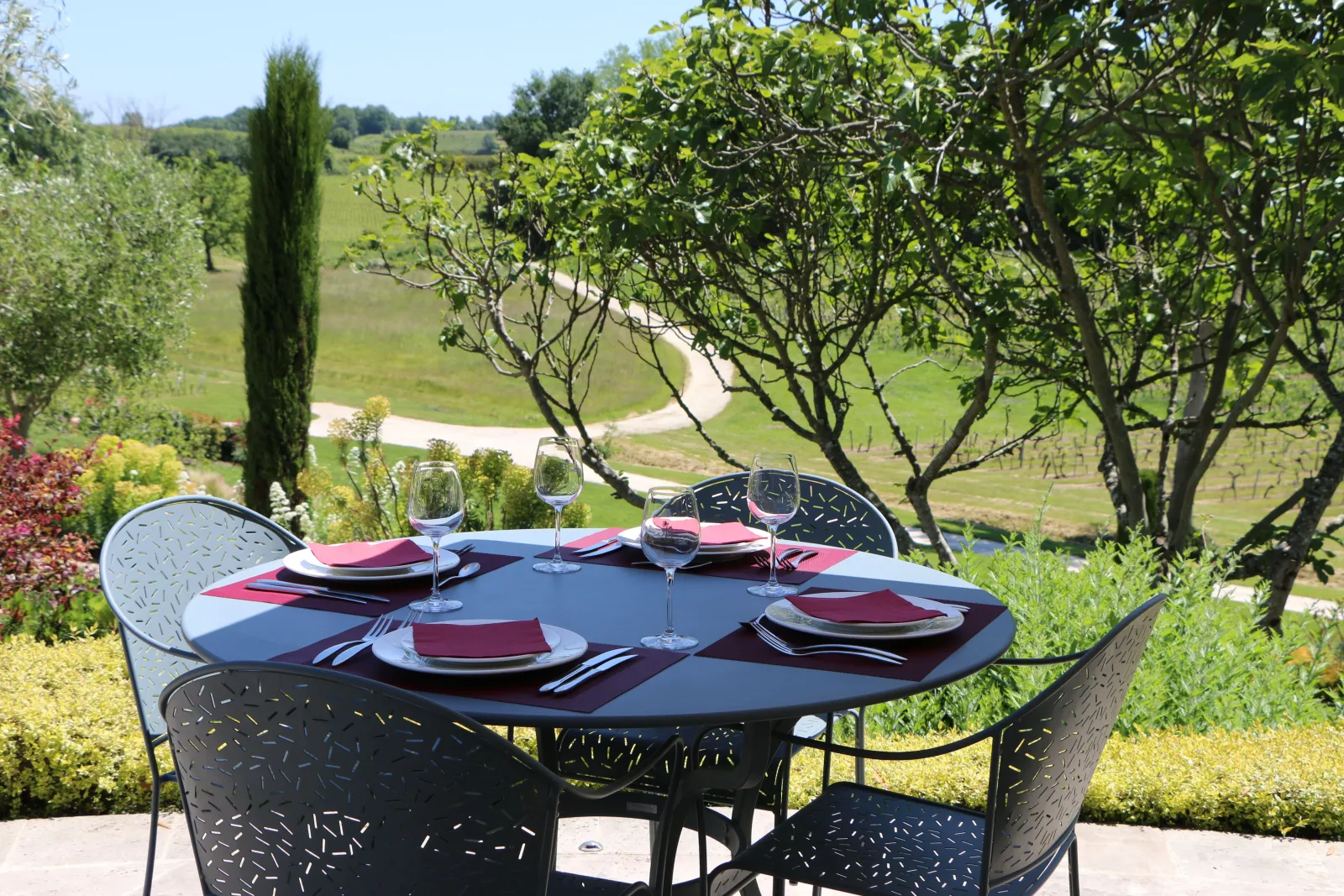 Elegant outdoor dining table set with burgundy and black tableware, overlooking lush vineyards at Château La Rose Perrière near Bordeaux.