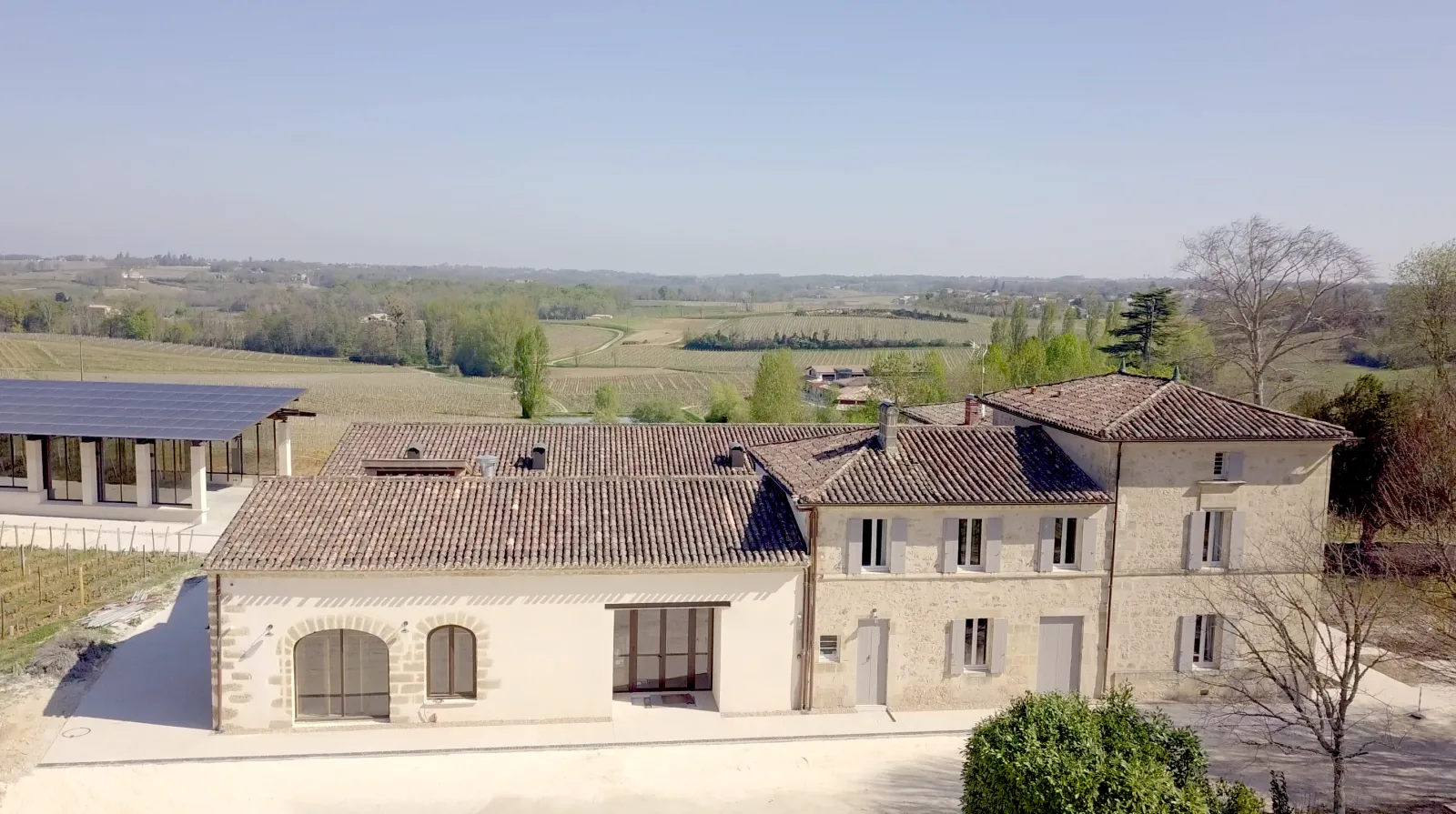 Aerial view of Logis de Valandraud near Bordeaux, featuring stone buildings with tiled roofs, solar panels, surrounded by vineyards and rural landscape.