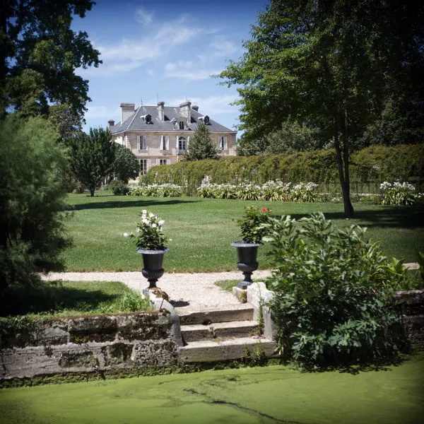 View of Château Kirwan in Bordeaux from the gardens, with its pink stone facades surrounded by lush greenery and flowering gardens
