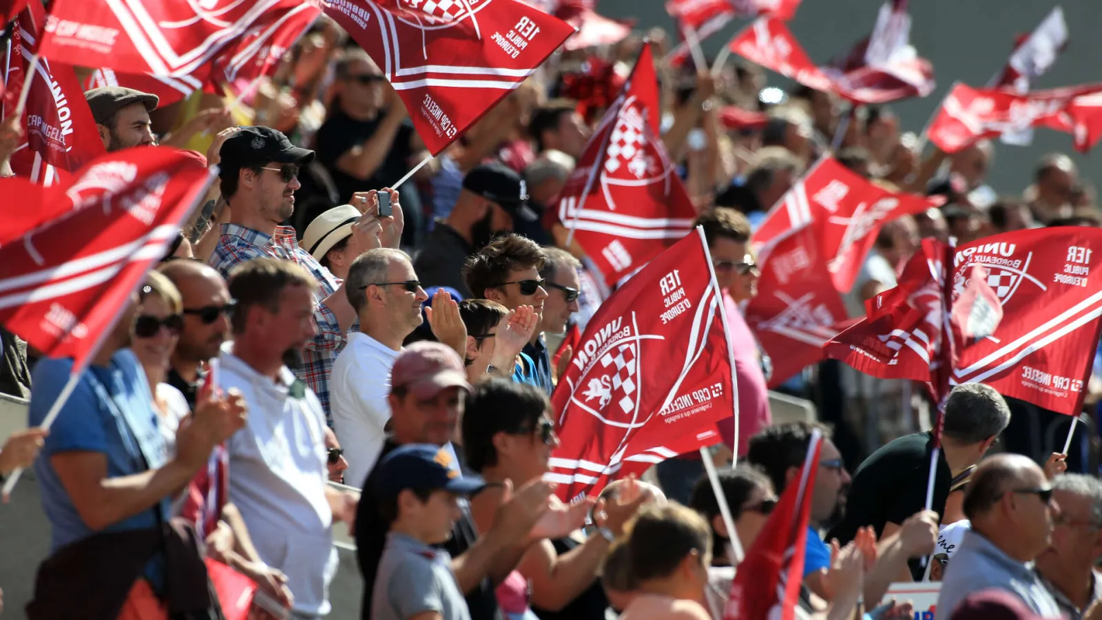 Crowd of supporters waving red and white flags at Chaban-Delmas Stadium in Bordeaux during a sporting event.