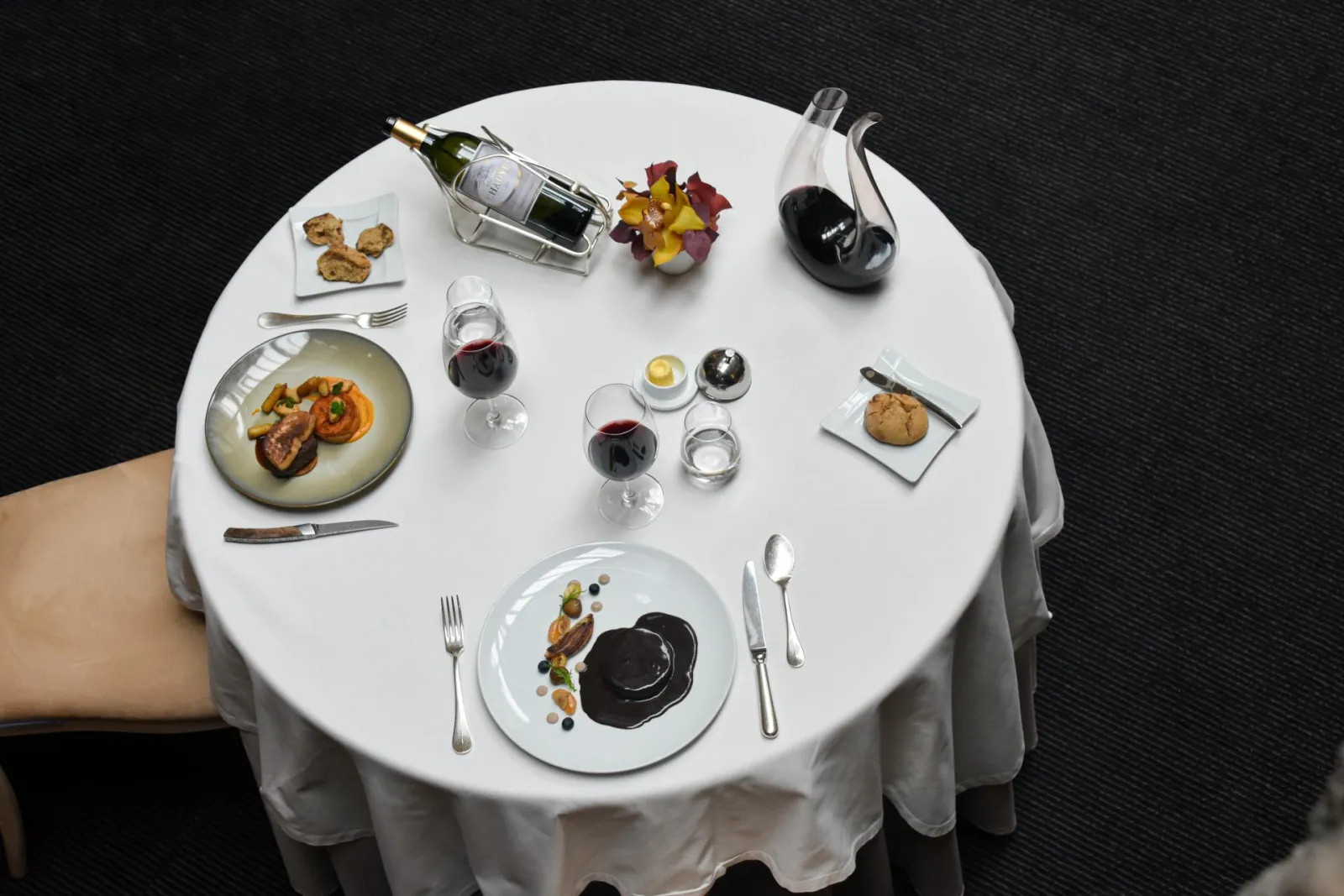 Elegant round table at Chapon Fin restaurant in Bordeaux, set with two place settings, refined cuisine, red wine glasses, white wine bottle, water carafe and floral decoration.