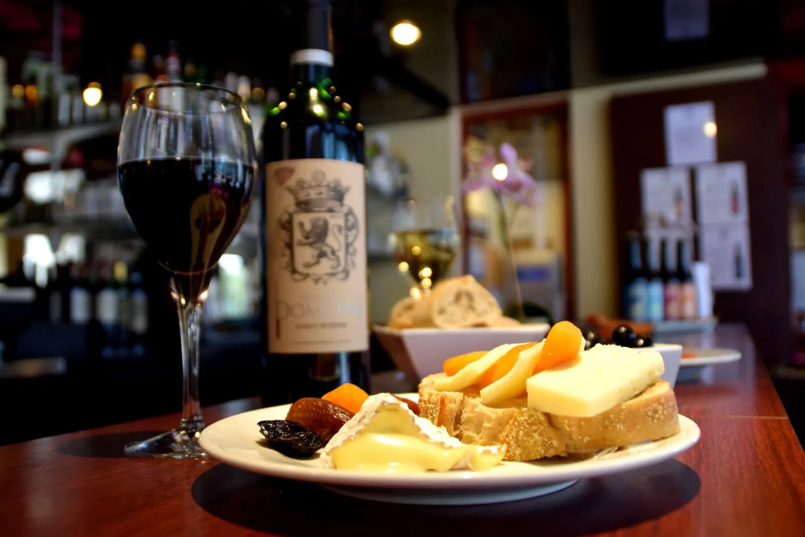 Glass of red wine, Bordeaux bottle, and charcuterie plate with cheese, toasted bread, and dried fruits in a Bordeaux restaurant