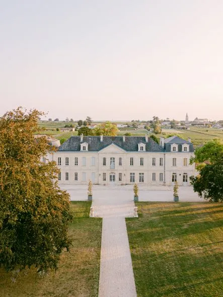Aerial view of Château Soutard, an elegant white manor house with blue slate roofs and a central paved pathway, surrounded by manicured gardens and Bordeaux vineyard landscapes