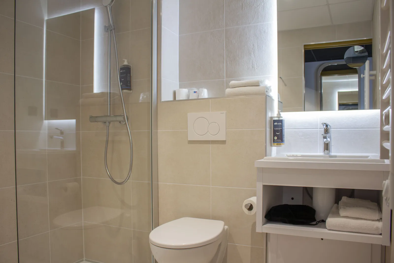 Modern bathroom with walk-in shower, toilet, white sink and illuminated mirror in a hotel room