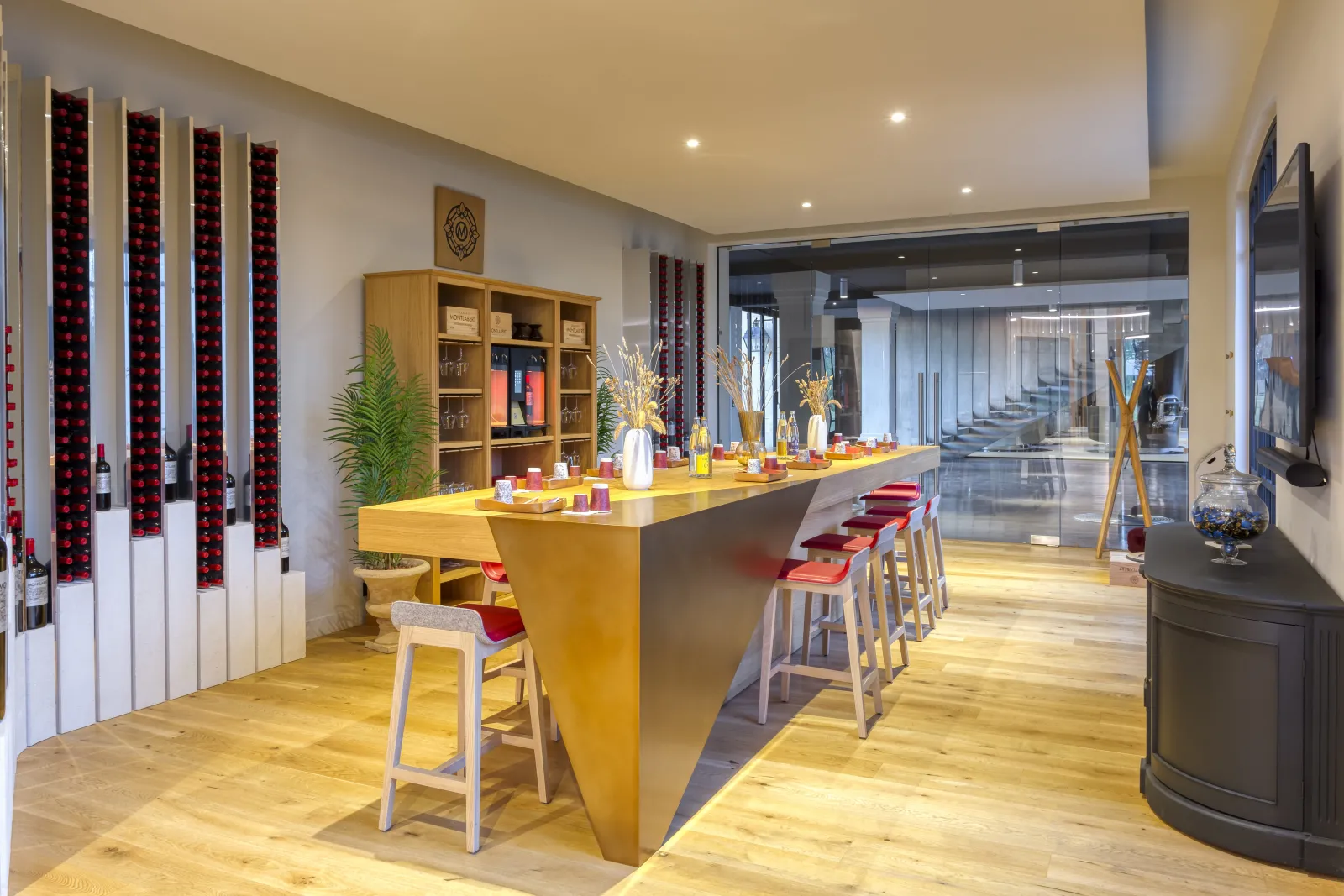 Elegant tasting room at Château Montlabert in Bordeaux featuring a yellow counter, red chairs, wine displays, and views through glass panels